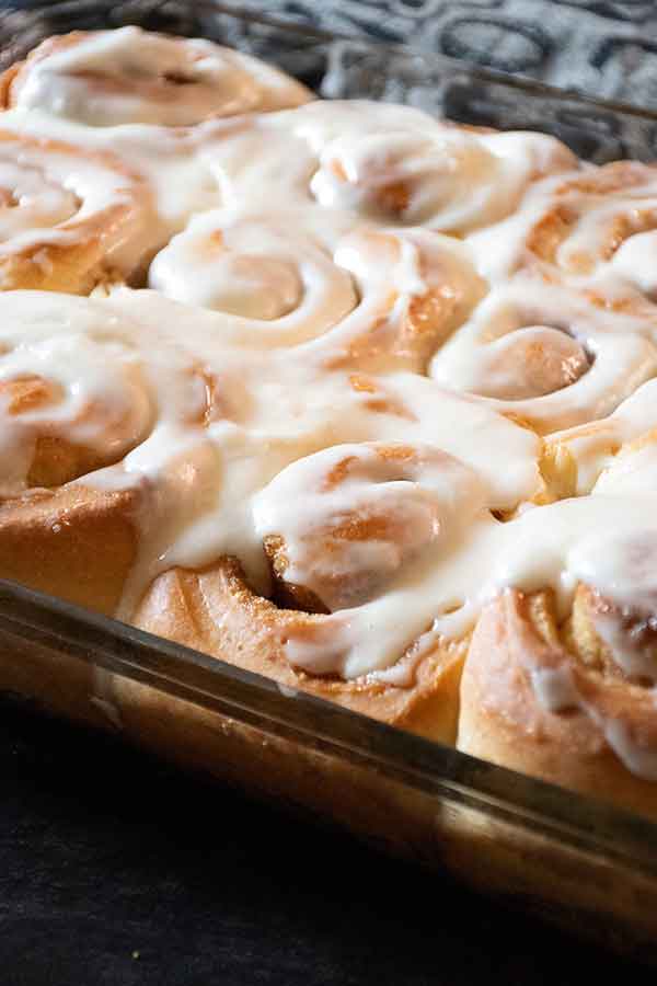 Side view of cinnamon rolls in a glass dish, showcasing their golden brown edges and a thick layer of icing.