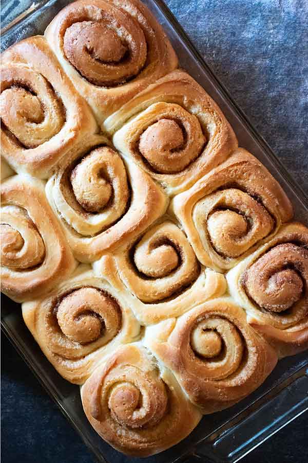 Overhead shot of unfrosted cinnamon rolls arranged tightly in a glass baking dish, revealing their neat spirals.