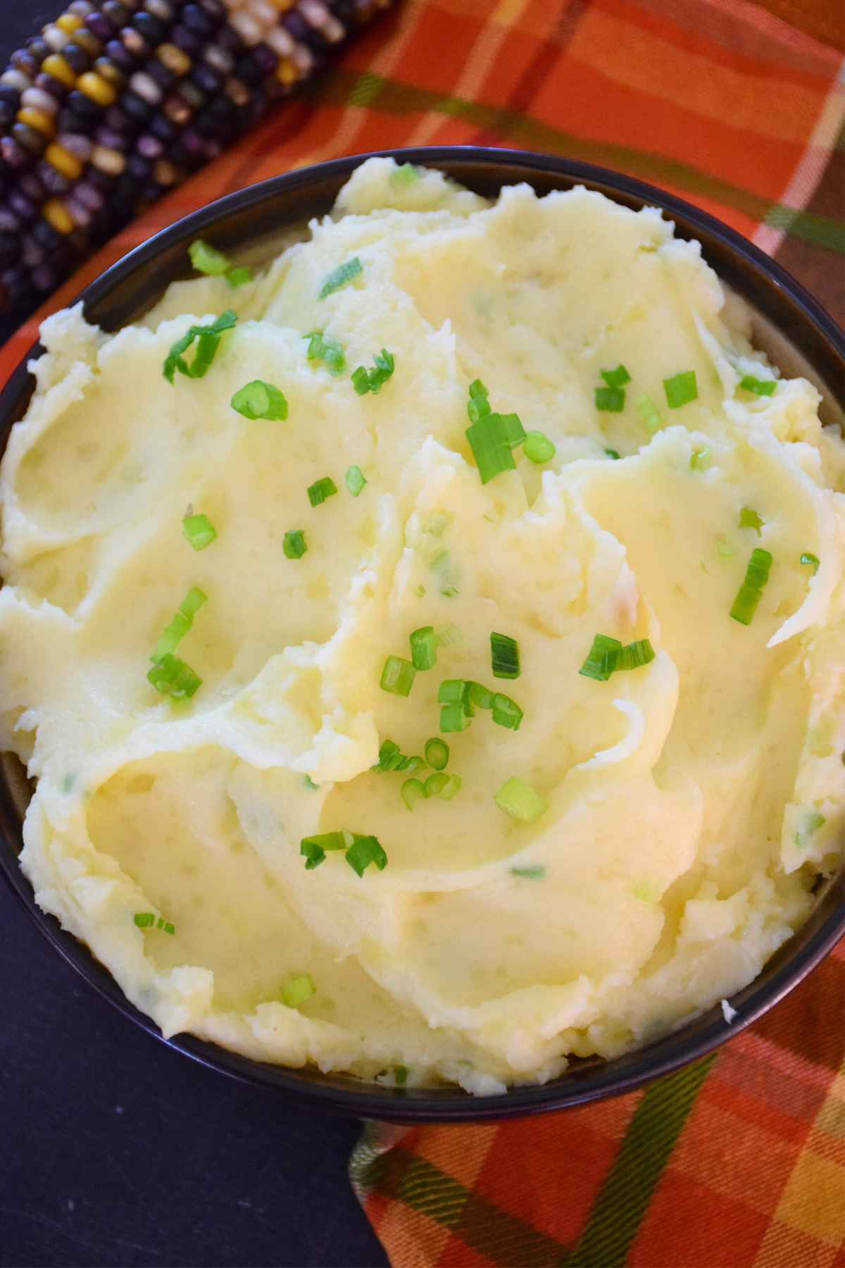 Top down view of mashed potatoes in a black bowl, sprinkled with chopped green chives and surrounded by fall themed decor.