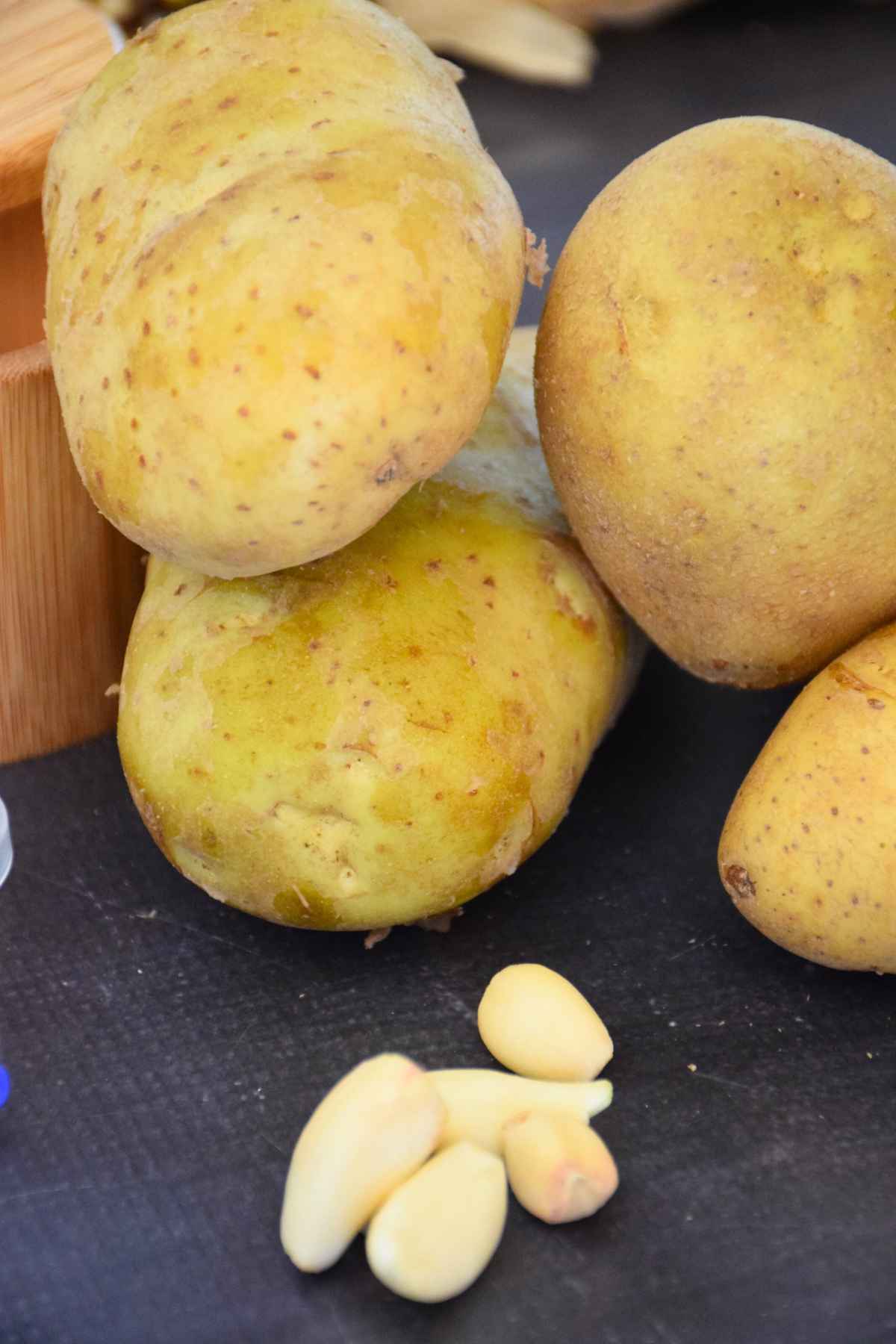 Whole yellow potatoes and peeled garlic cloves on a dark surface.