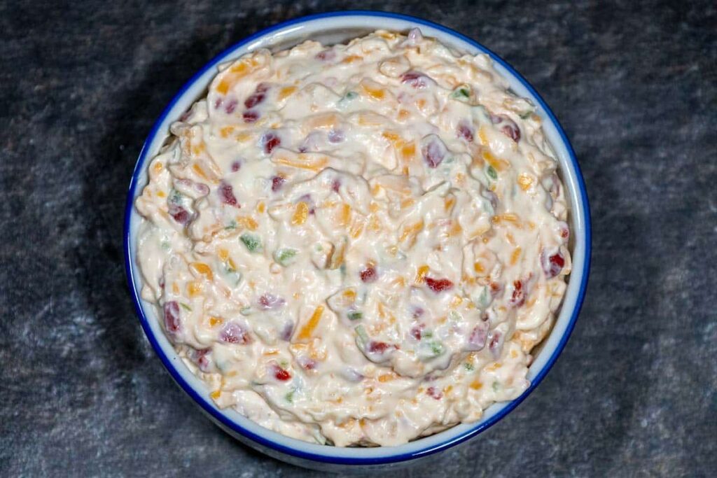 Top down view of bowl filled with jalapeno pimento cheese spread, showing a creamy mixture of shredded cheddar, diced pimentos, and green jalapenos blended with mayonnaise and cream cheese in a blue rimmed bowl.