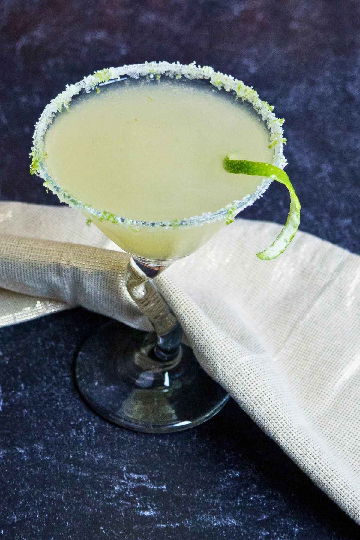 Lime green colored drink with a sugary and lime zest rim in a martini glass.