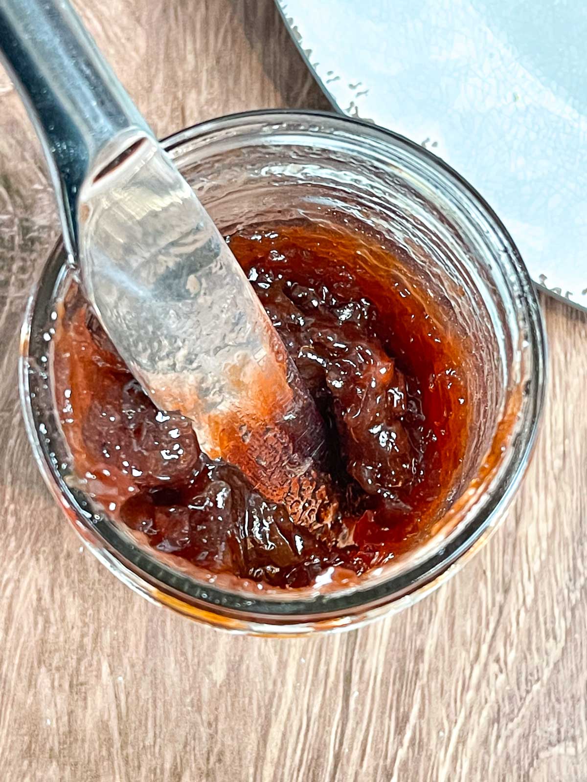 A knife resting inside a mason jar of thick muscadine jam, viewed from above.