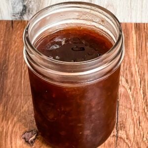 Jar filled with dark, glossy muscadine jam sitting on a wooden surface.
