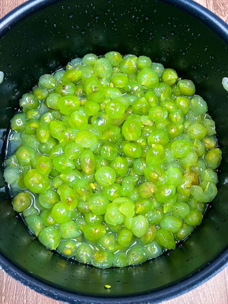 A pot filled with bright green muscadine grape interiors after the skins have been removed, glistening in their juice.