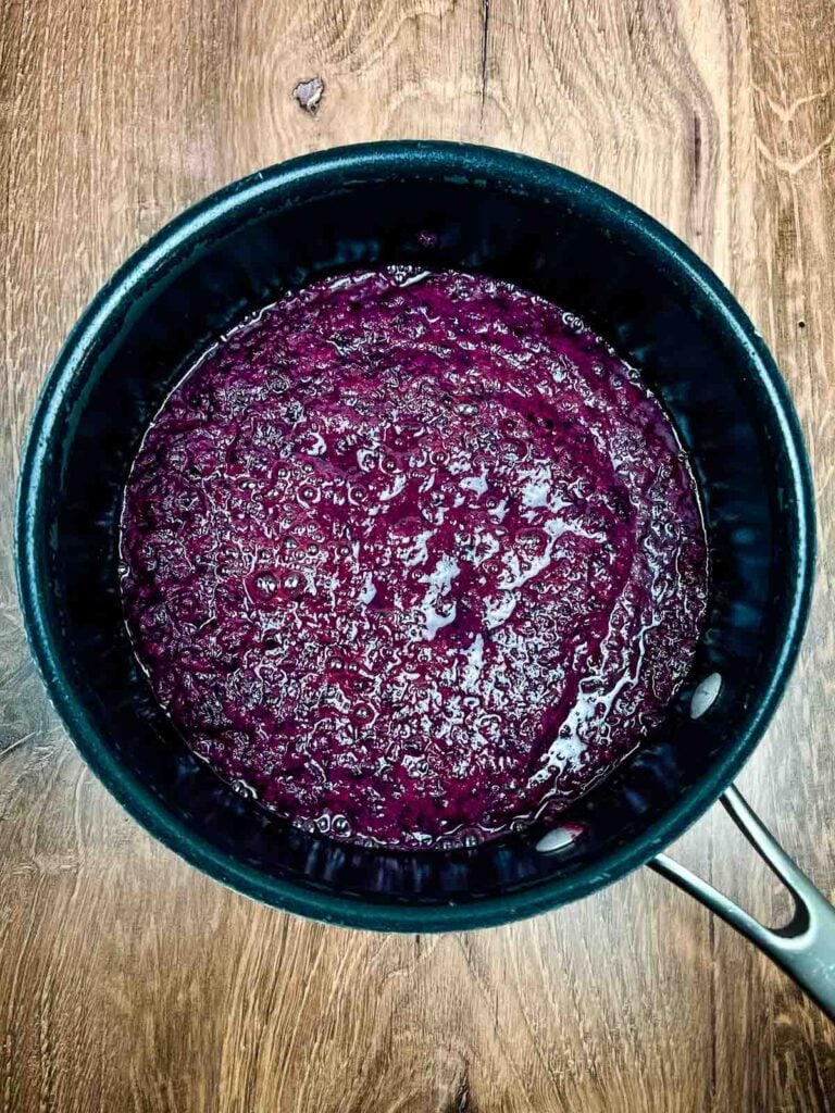 A pot of simmering pureed muscadine grape skins forming a deep purple mixture.