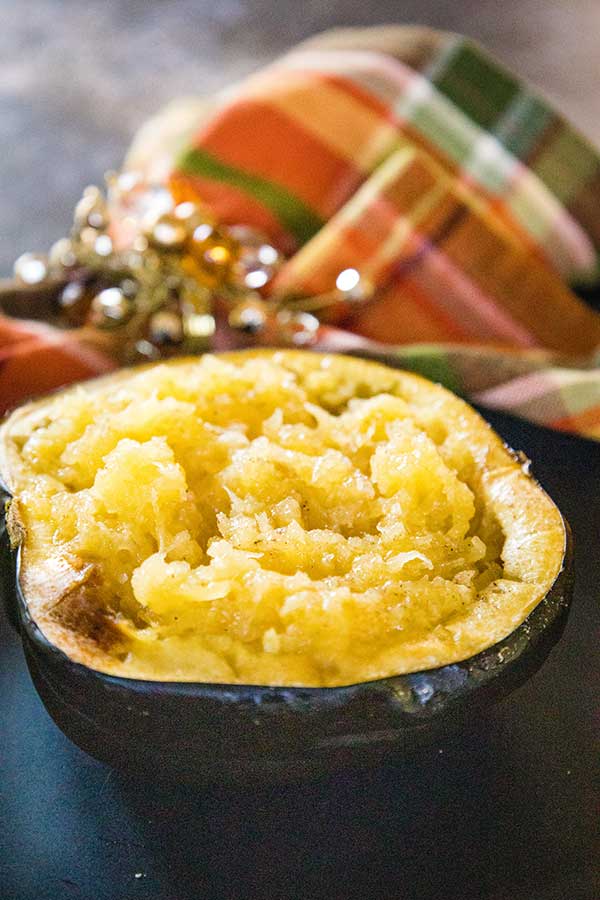 Roasted mashed acorn squash served in it's shell on a black plate with a fall-themed plaid napkin in the background.