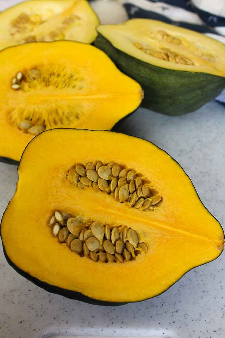 Raw acorn squash havles showing bright orange flesh and seeds arranged on a countertop.