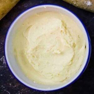 Overhead view of a bowl of salted maple butter on a dark countertop surrounded by slices of rustic bread.