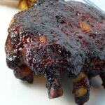 A rack of baby back ribs coated in dark, sticky barbecue sauce on a white plate.
