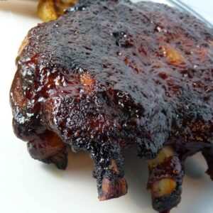 A rack of baby back ribs coated in dark, sticky barbecue sauce on a white plate.