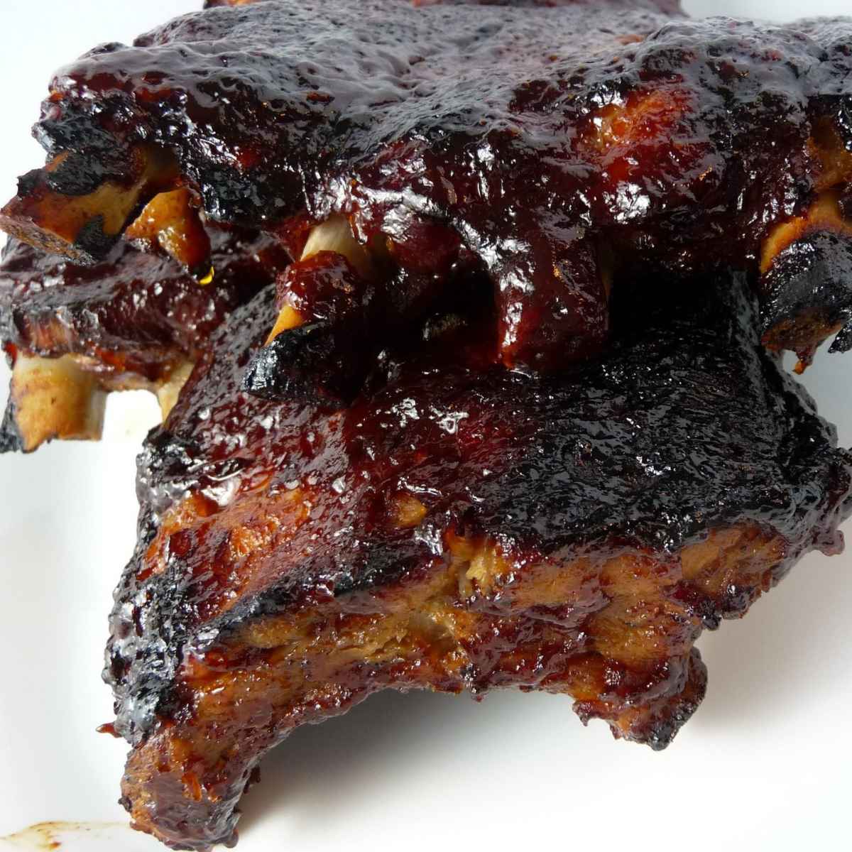 A pile of saucy slow cooker baby back ribs with dark charred edges and a glossy glaze.