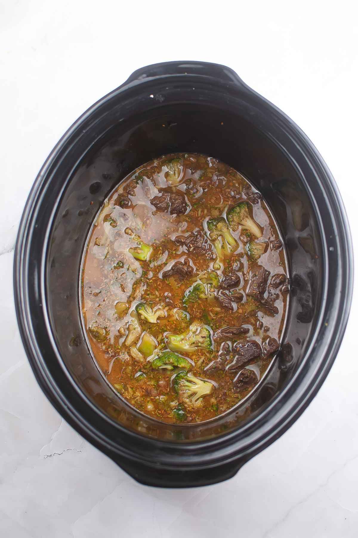 Overhead view of a slow cooker filled with beef teriyaki and broccoli in a simmering sauce.
