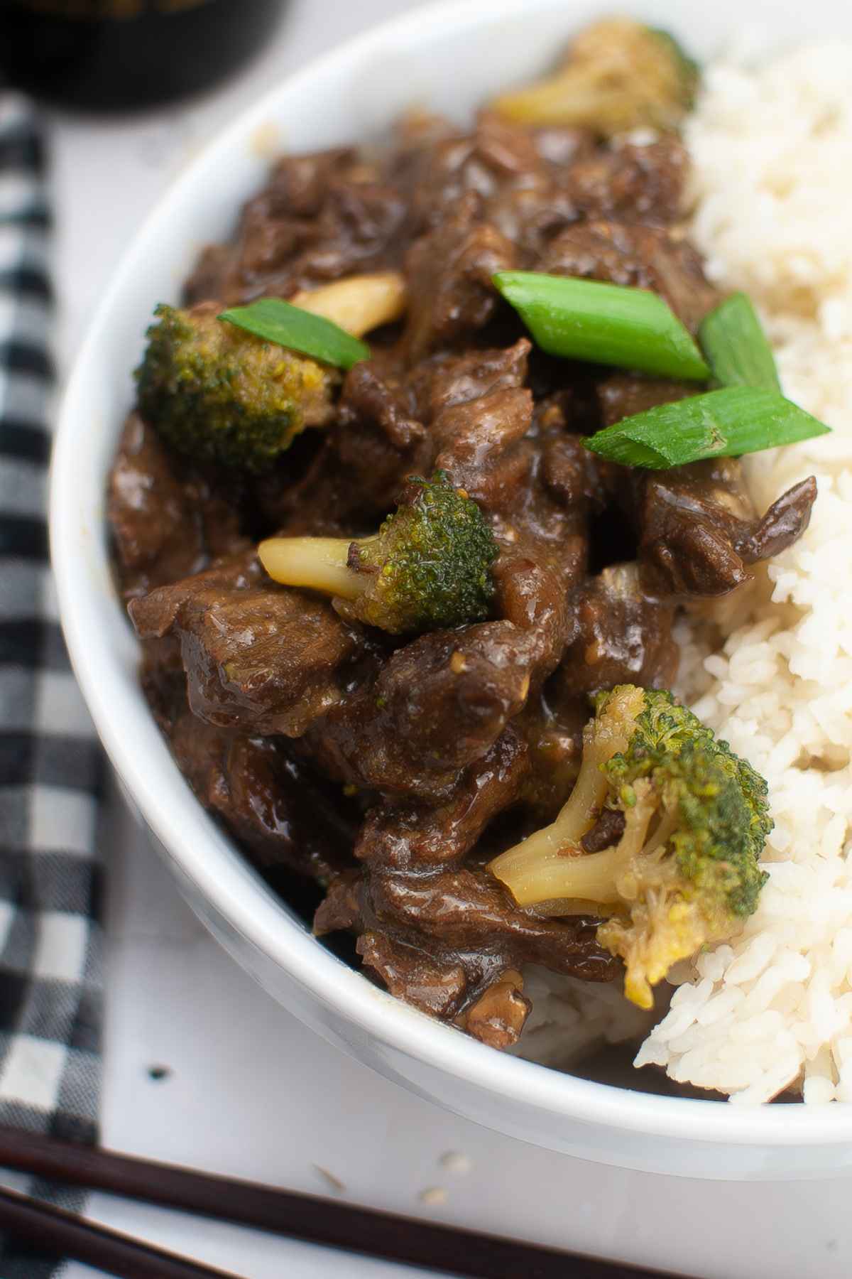 Extreme close up of beef teriyaki with broccoli and green onion on top of rice, showcasing the thick, savory sauce coating the meat.