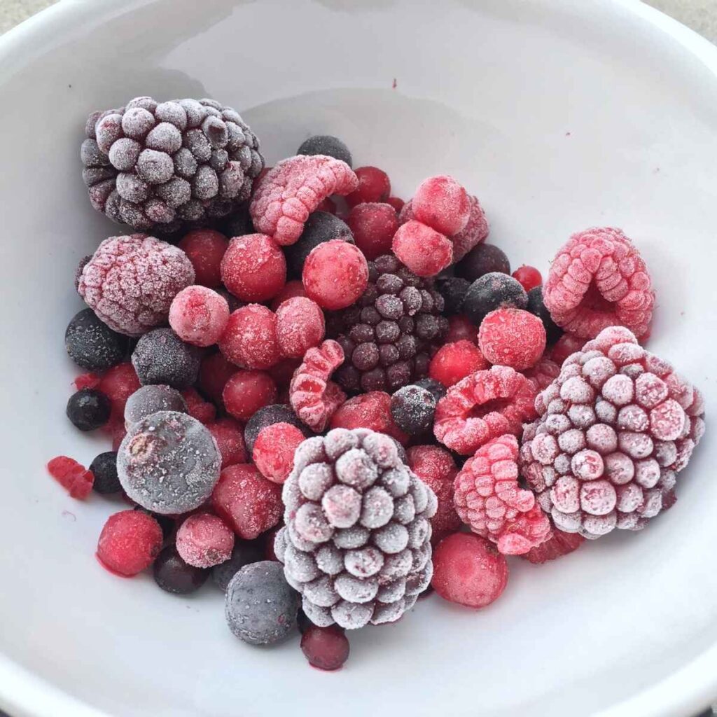 A white bowl filled with a variety of frosty mixed berries, including blackberries, raspberries and blueberries.