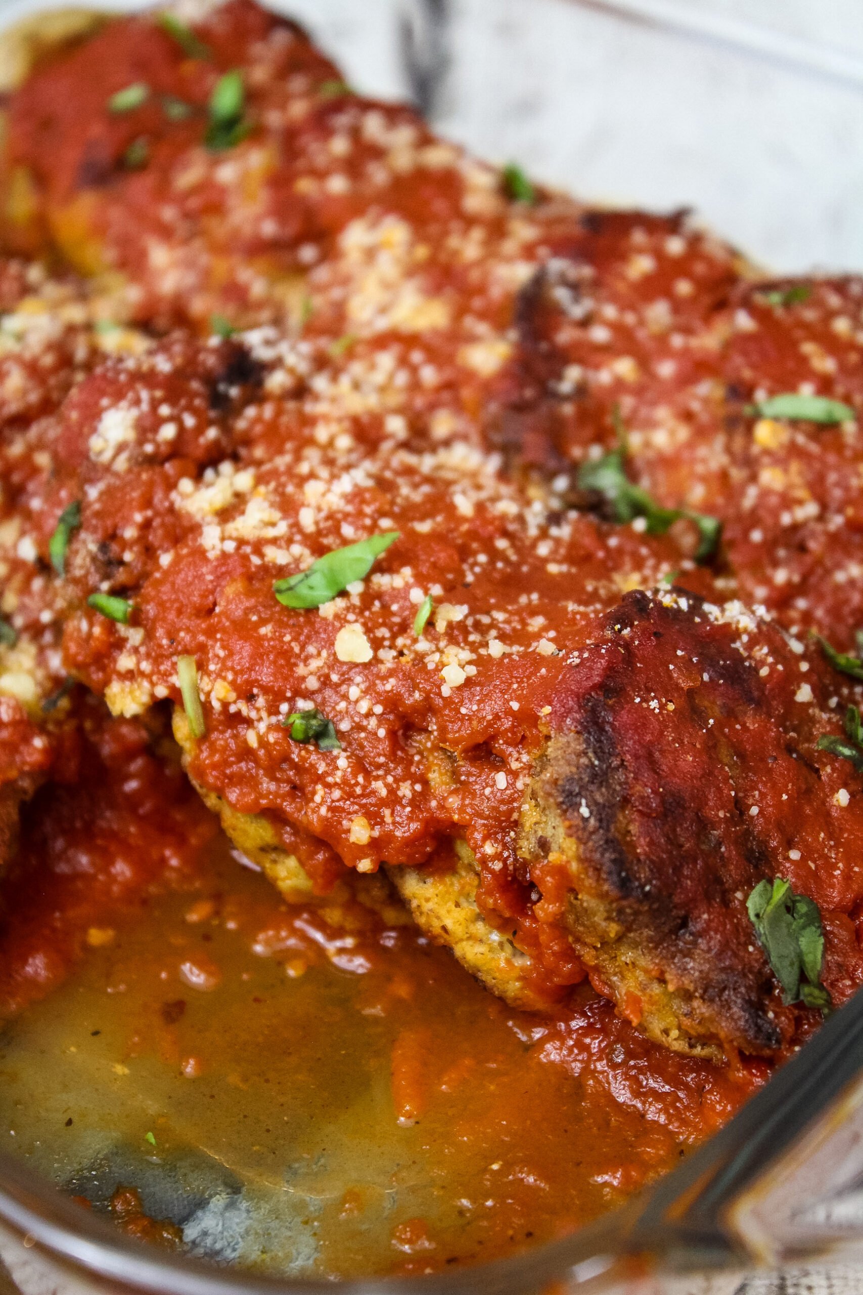 Baked vegetarian meatballs in a glass dish, covered in marinara sauce, garnished with chopped basil and grated parmesan.