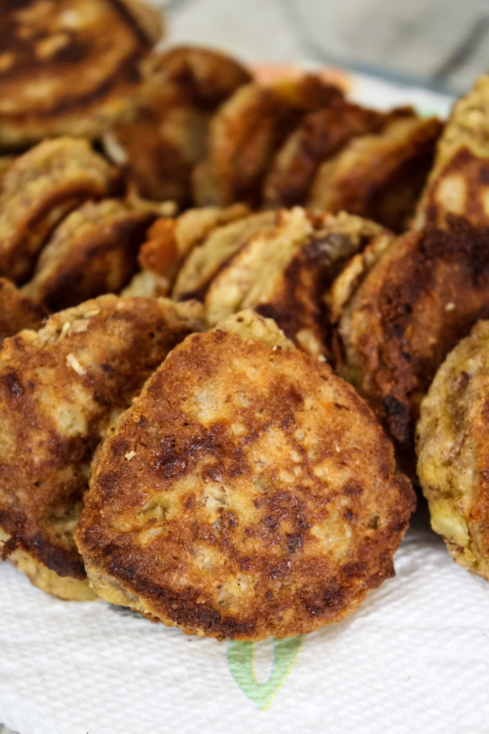 Stacks of crispy vegetarian patties resting on a paper towel, showing golden brown, pan-fried surfaces.