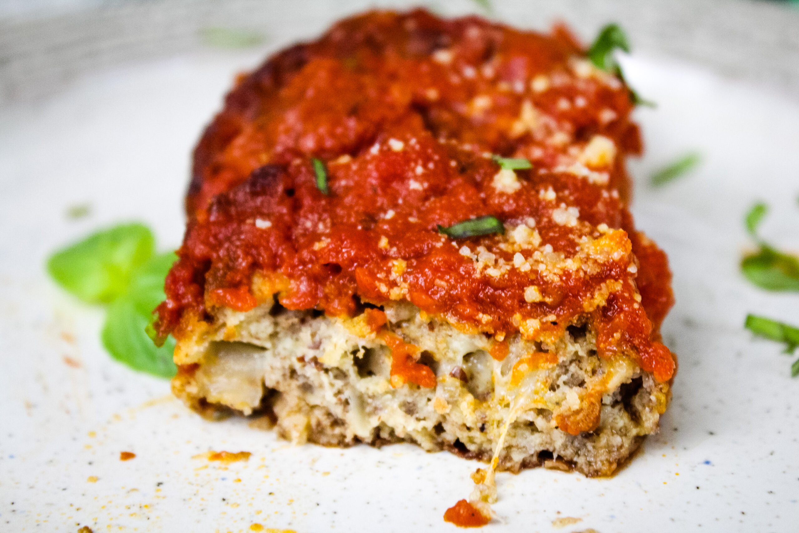 Close up of a sliced vegetarian meatball on a plate, revealing a cheesy and hearty interior beneath marinara sauce.