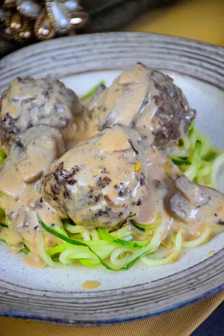 Three venison meatballs topped with creamy Alfredo mushroom sauce, served over a bed of zucchini noodles on a ceramic plate.