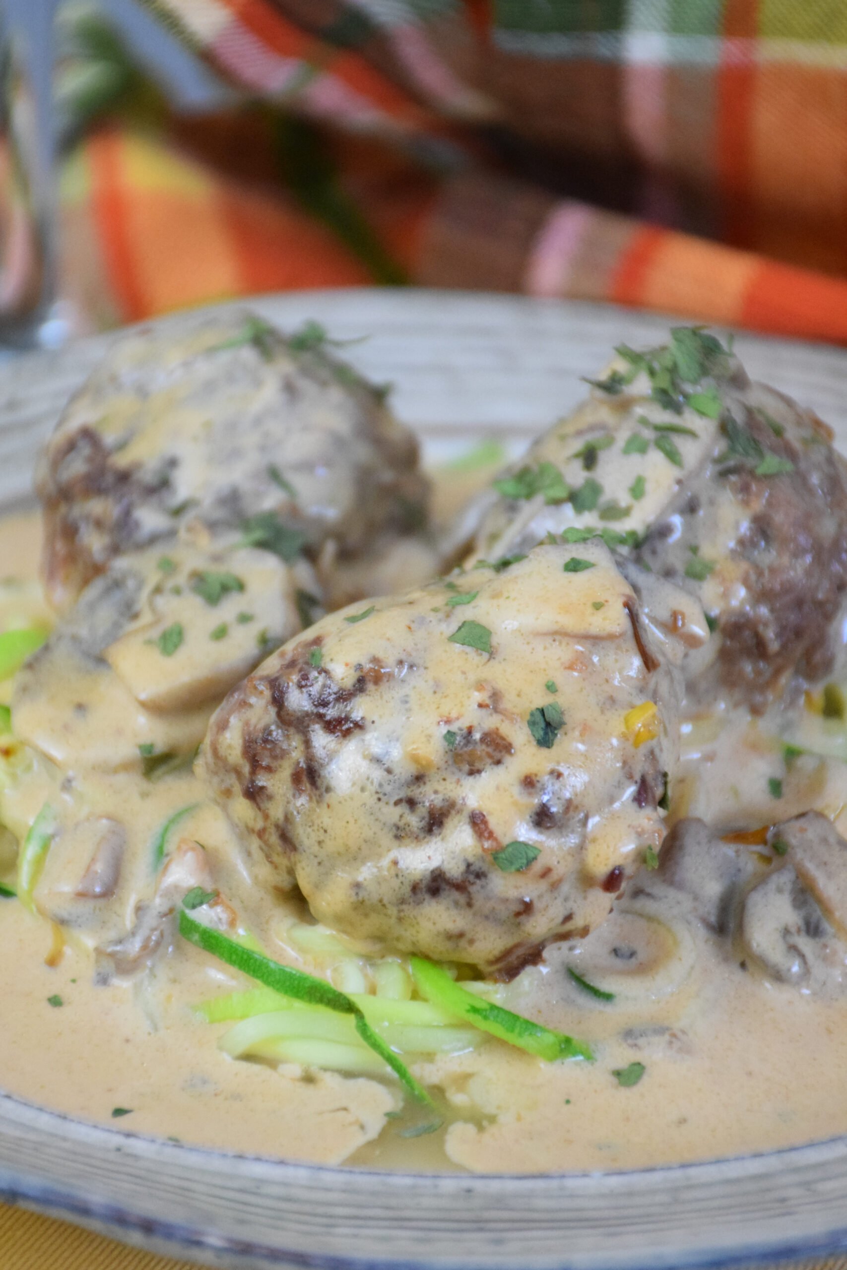 Close up of venison meatballs served over zucchini noodles and smothered in a creamy Alfredo mushrooms sauce, garnished with chopped herbs.