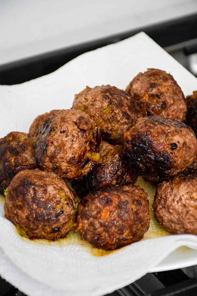 Freshly cooked meatballs resting on a paper towel lined plate, showing a browned and slightly crispy exterior.