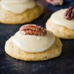 Soft Butternut Squash Cookies topped with creamy brown sugar frosting and a pecan half, arranged on a dark surface.