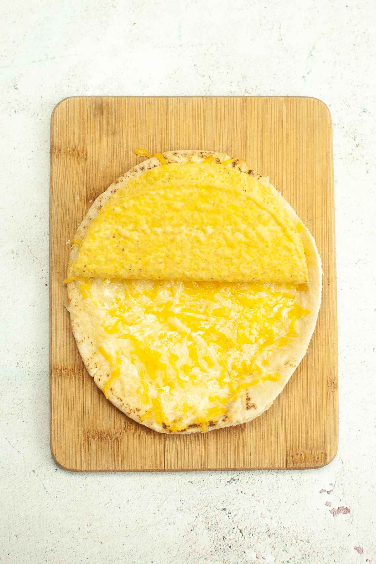 A hard taco shell pressed onto melted cheese on flatbread.