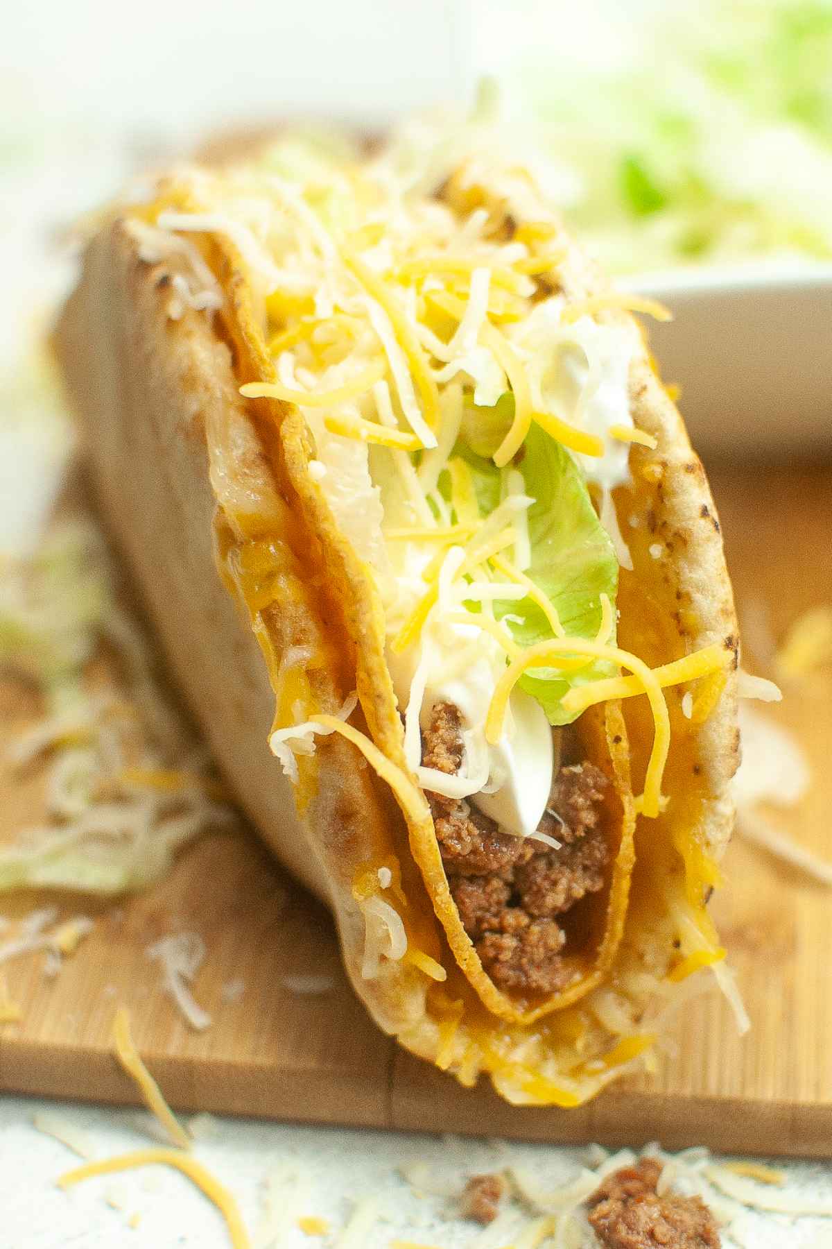 Close up of a cheesy gordit crunch taco with ground meat, shredded lettuce, sour cream, and cheese inside a crispy shell wrapped in soft flatbread.