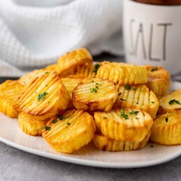 A plate of golden brown accordion potatoes garnished with chopped parsley served on a white plate with a soft gray background.