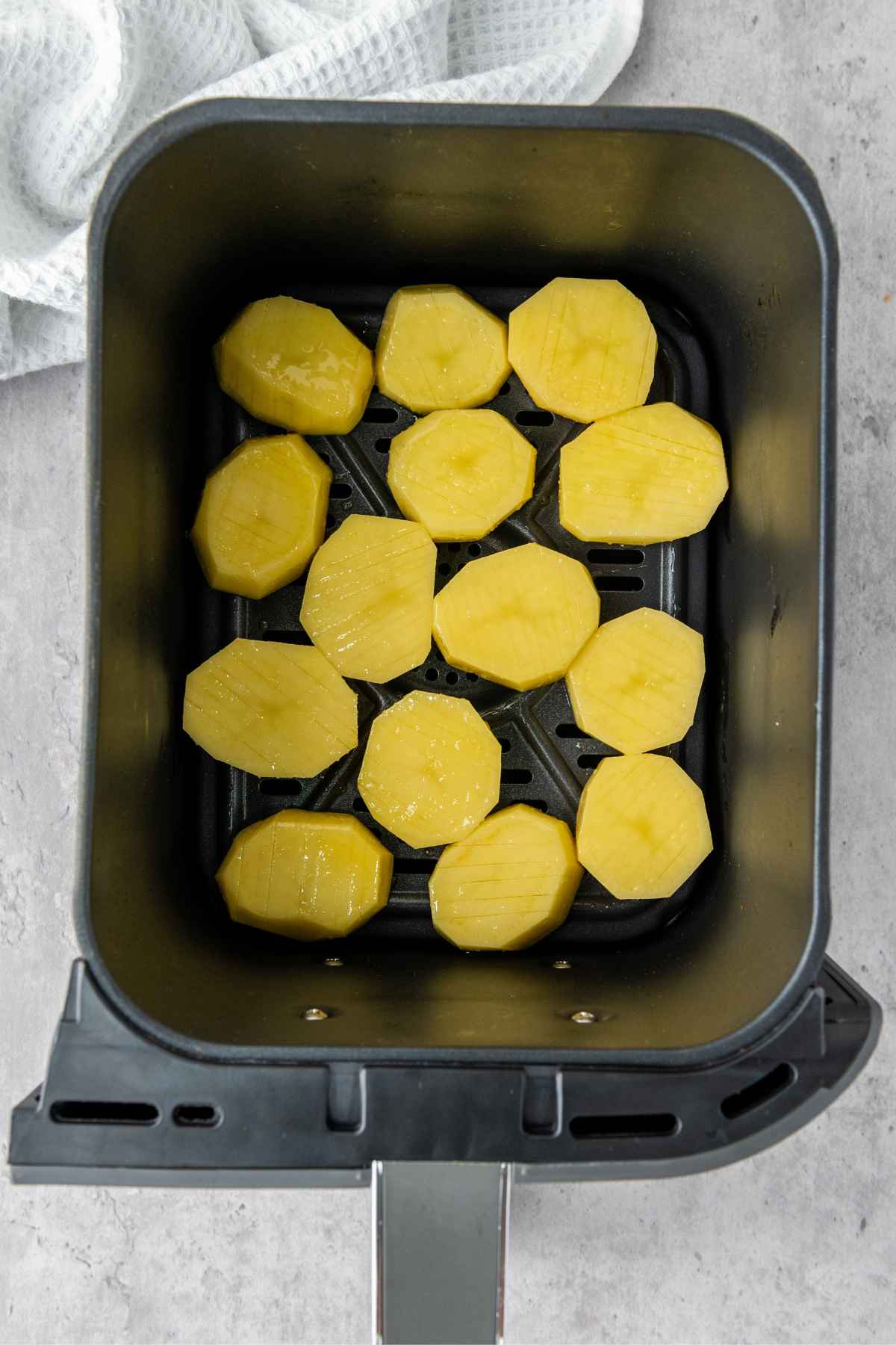 Raw sliced accordion cut potatoes placed in a single layer inside an air fryer basket.