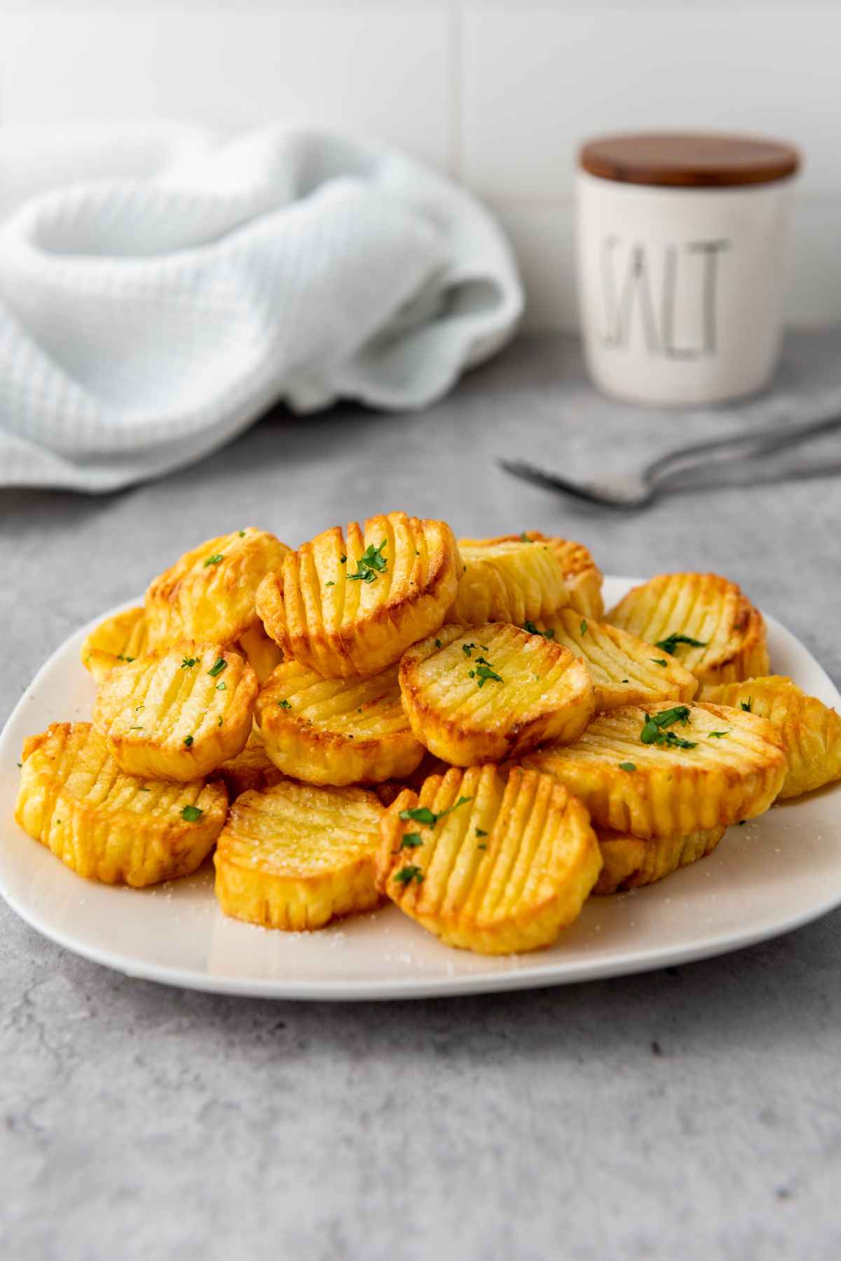 A plate of golden brown accordion potatoes garnished with chopped parsley served on a white plate with a soft gray background.