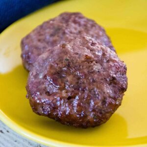 Two Air Fryer Breakfast Sausage Patties on a yellow plate.