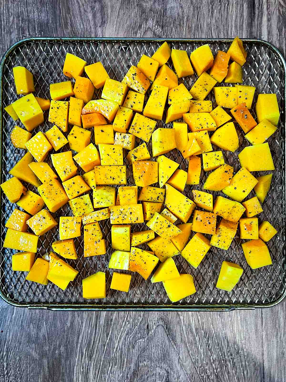 An air fryer tray with diced butternut squash seasoned with salt and pepper.