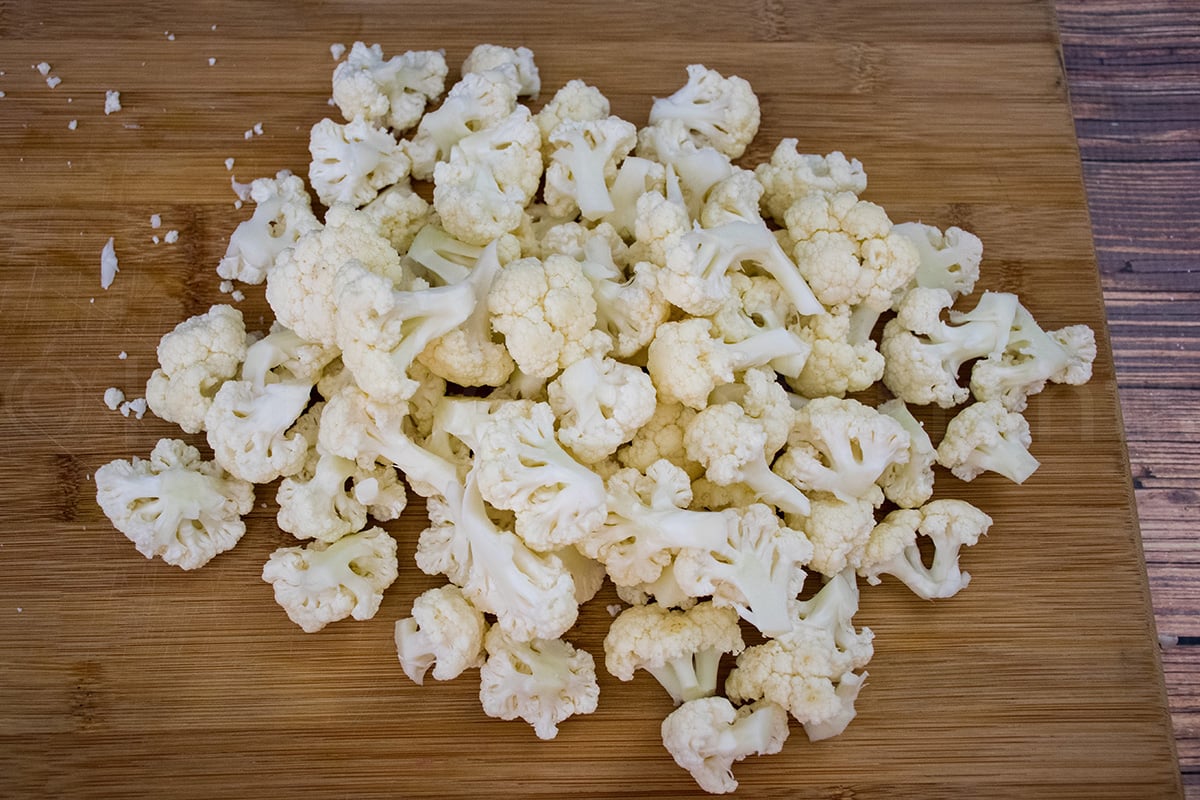 Raw cauliflower florets spread out on a wooden cutting board, ready for cooking.