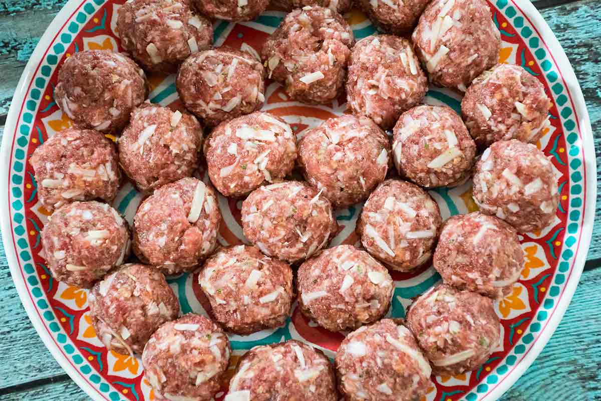 A large colorful plate filled with raw venison meatballs, showing shredded cheese and onion in the mix.