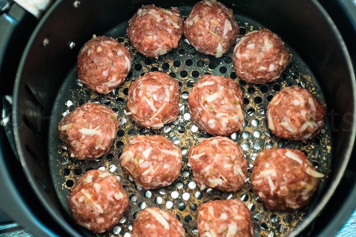 Raw venison meatballs arranged in a single layer in the basket of an air fryer, ready for cooking.