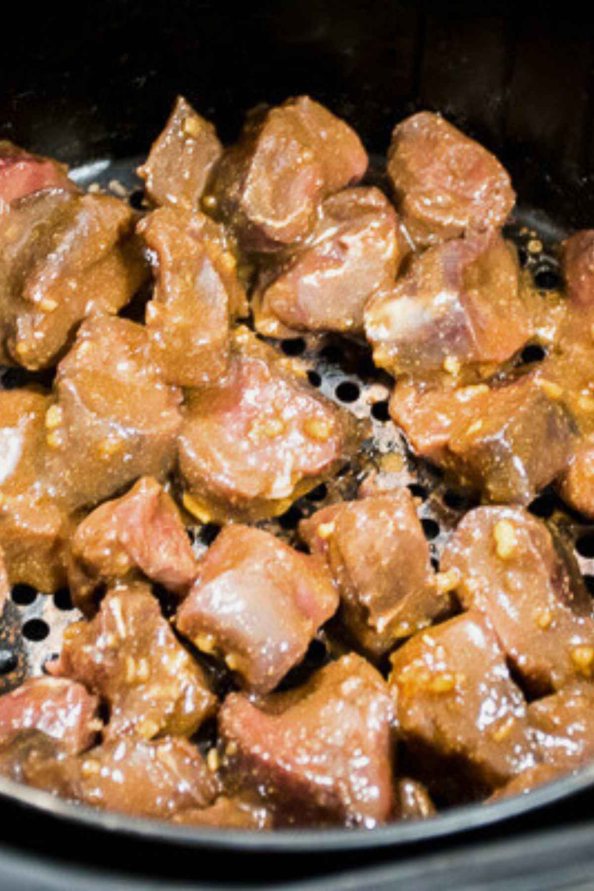 Cubed venison steak tenderloin bites marinated and arranged in an air fryer basket, ready to be cooked.