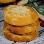 A stack of three golden brown keto asiago bagels on a rustic white board with a red, yellow, and green towel in the background.
