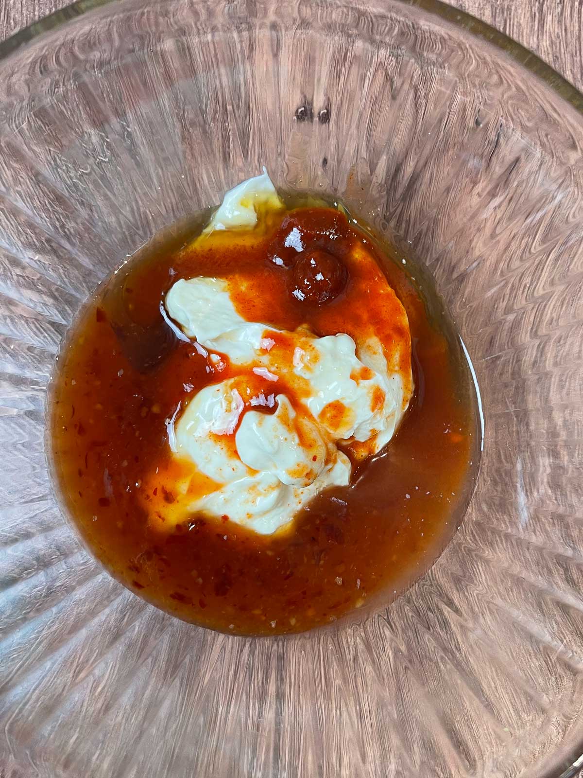 A glass mixing bowl filled with mayonnaise, Thai sweet chili sauce, honey, sriracha, and rice vinegar before being stirred together.