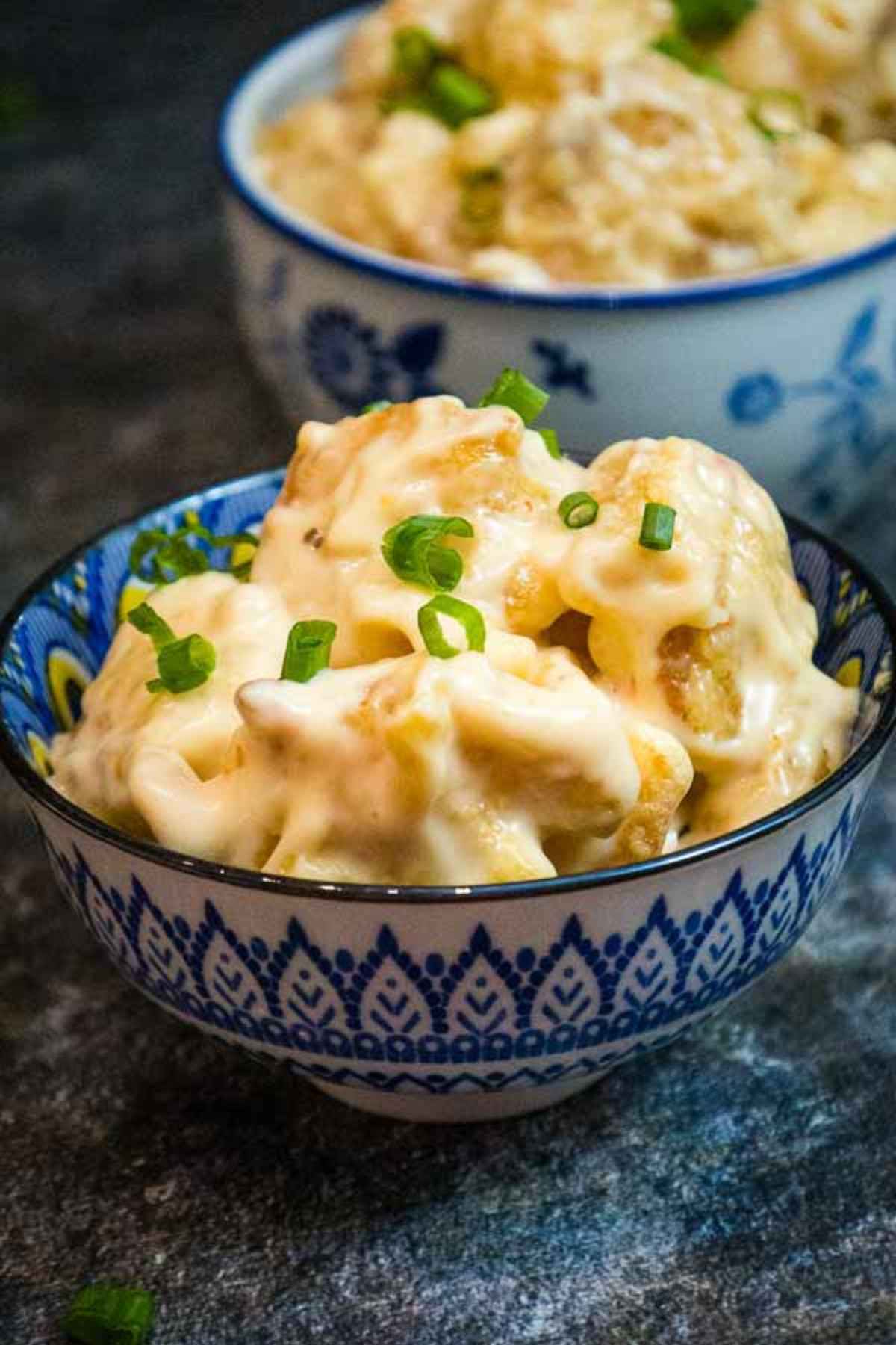 A close up of blue and white patterned bowl filled with bang bang shrimp coated in creamy sauce and topped with green onions, with a second bowl of shrimp in the background.