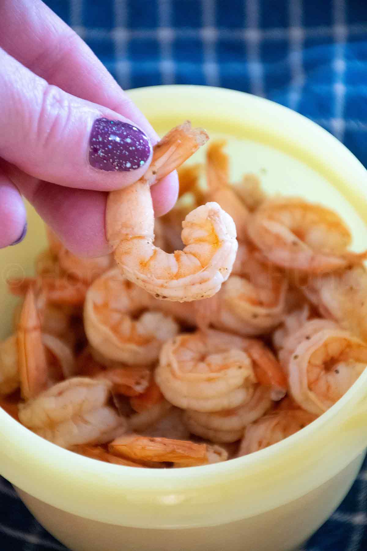 Old Bay Boiled Shrimp in a yellow bowl with a hand with glittery nail polish holding a piece of the shrimp outside of the bowl.