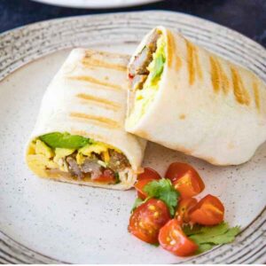 Two halves of a grilled breakfast burrito on a plate, served with cherry tomato halves and a sprig of fresh cilantro.