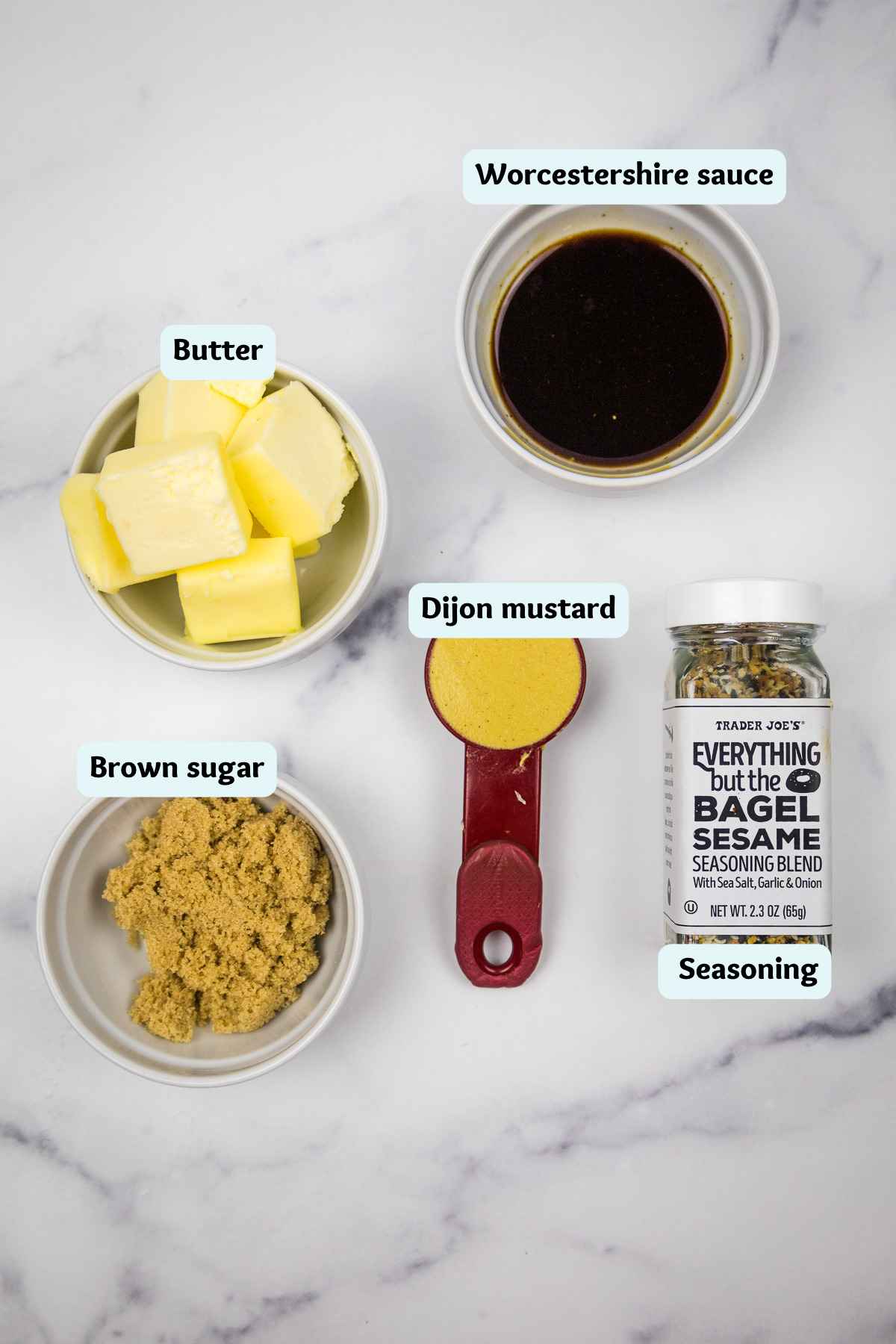 Labeled ingredients for a savory butter topping on a white marble background, including cubed butter, brown sugar, Dijon mustard, Worcestershire sauce, and Everything but the Bagel Seasoning.