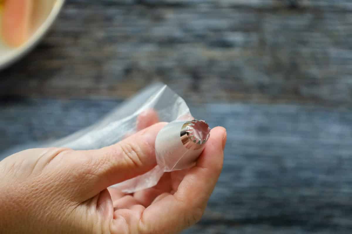 Close-up of a hand holding a piping bag fitted with a metal star tip, ready to pipe deviled egg filling.