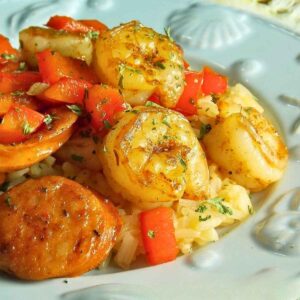 Close up of a plate of Cajun Shrimp and Chicken Sausage served over seasoned rice, topped with sauteed red bell peppers and garnished with herbs.