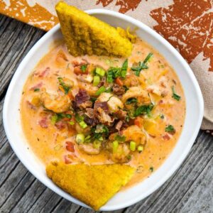 A close up top down view of a bowl of Cajun Shrimp in a creamy tomato-based sauce, garnished with scallions, parsley, and bacon bits, served with golden fried polenta wedges.