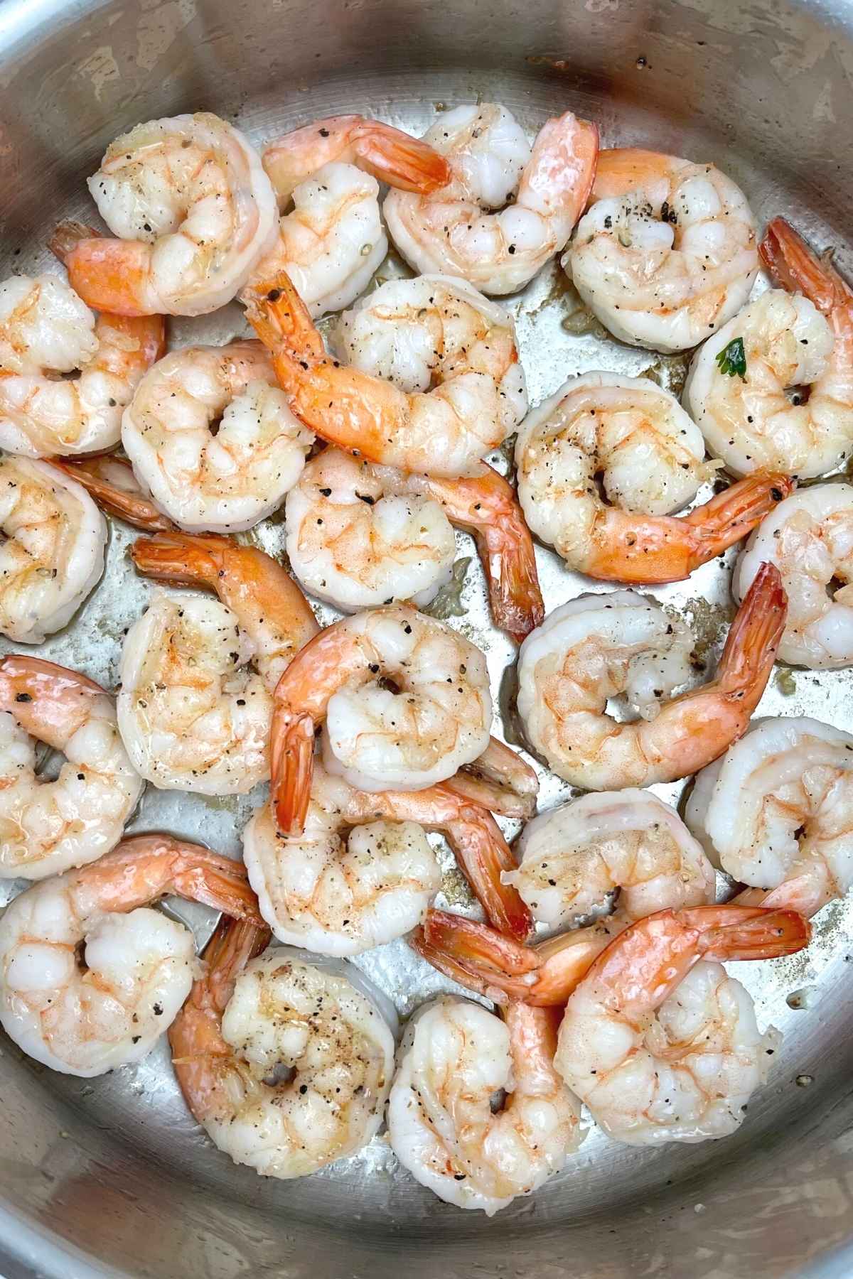 Lightly browned shrimp seasoned with black pepper in a stainless steel skillet.