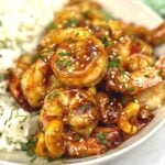 Plated cashew shrimp in a bowl with white rice, sesame seeds and fresh chopped parsley.