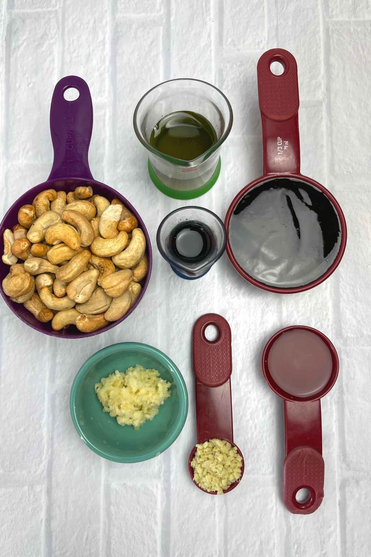 Overhead view of ingredients for cashew shrimp including cashews, minced garlic, soy sauce, and brown sauce in measuring cups.