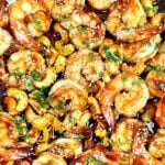 Cashew shrimp in a skillet coated in glossy sauce and sprinkled with sesame seeds and chopped herbs.